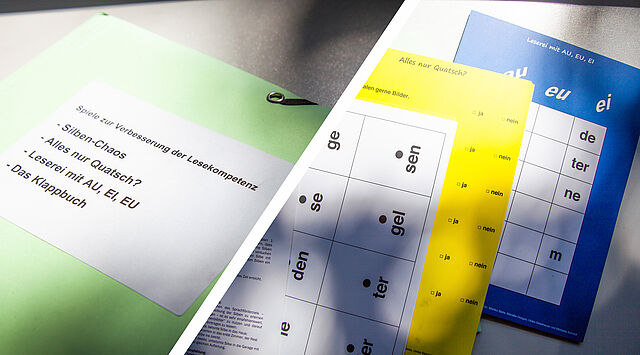 Grüne Mappe sowie Seiten mit Silbenspiel auf Tisch
