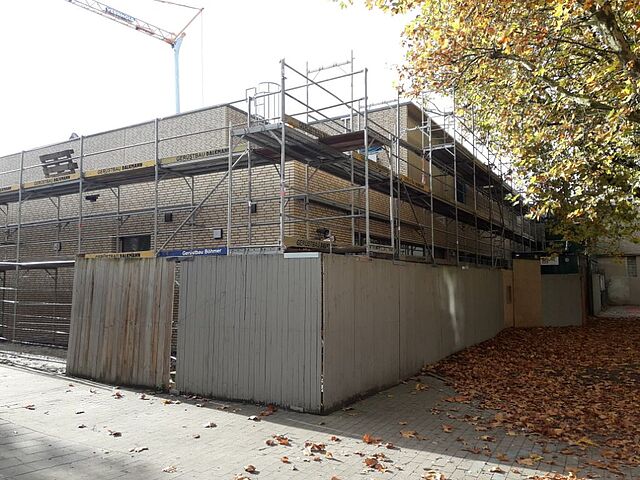 Neubau Turnhalle mit Gerüst hinter Bauzaun