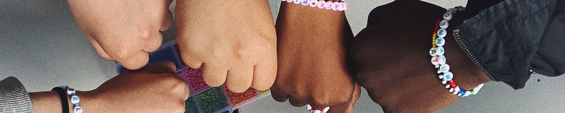 Acht Arme unterschiedlicher Hautfarbe und mit selbstgebastelten Armbändern geschmückt bilden einen Kreis. 