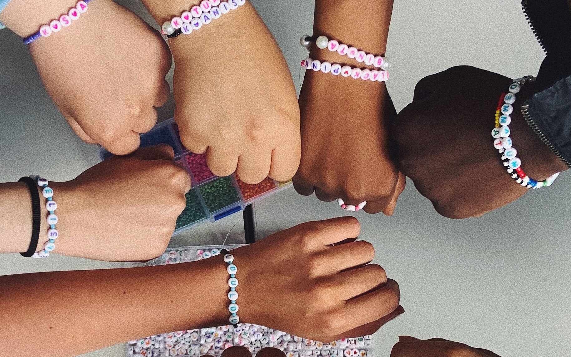 Acht Arme unterschiedlicher Hautfarbe und mit selbstgebastelten Armbändern geschmückt bilden einen Kreis. 