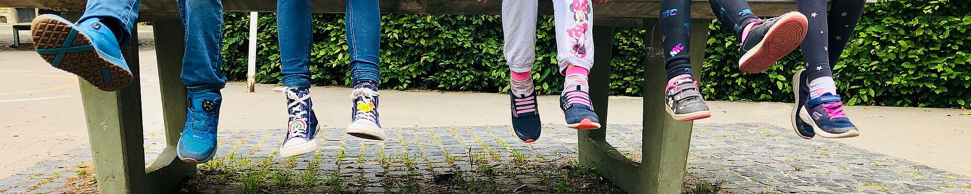 Fünf Rosenkinder sitzen auf einer Tischtennisplatte auf dem Schulhof und lassen die Beine baumeln.