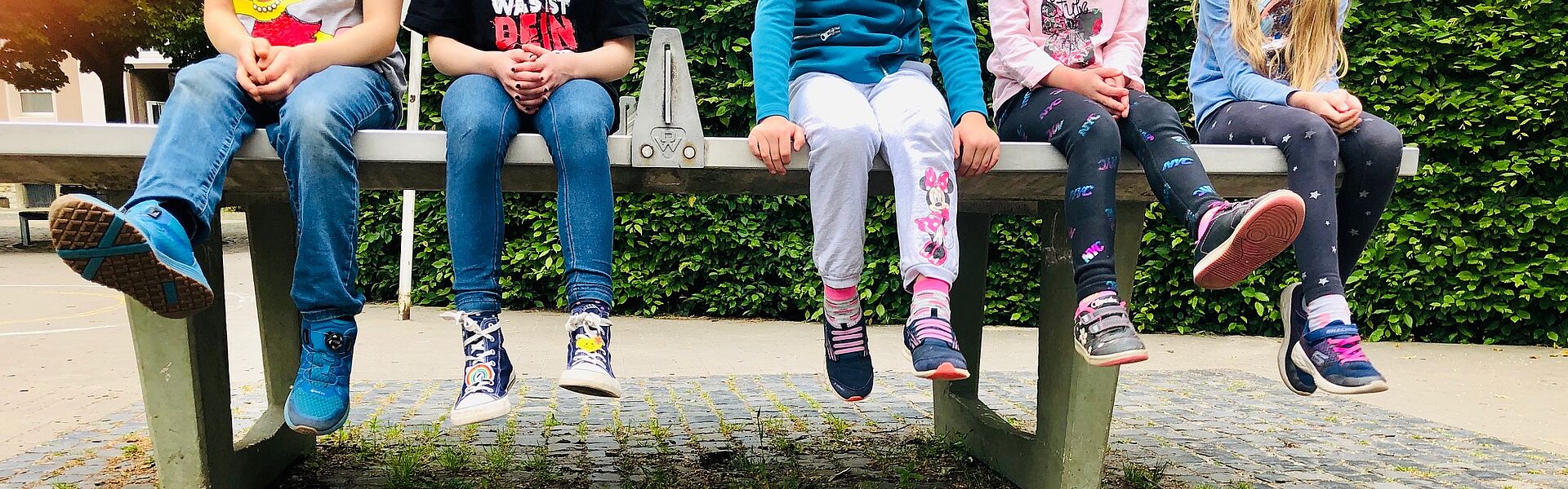 Fünf Rosenkinder sitzen auf einer Tischtennisplatte auf dem Schulhof und lassen die Beine baumeln.