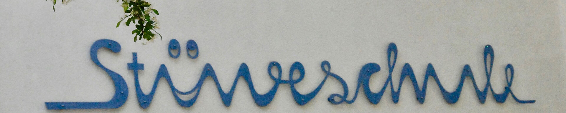 Ein Foto von Schriftzug der Stüveschule auf dem Schulgebäude. Im Vordergrund sind Äste mit grünen Blättern.